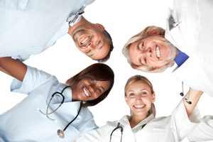 Four smiling Medical Professionals are standing in a circle, looking down at the camera, and smiling