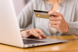 A women is sitting at a desk with an open laptop and a debit or credit card in her hand